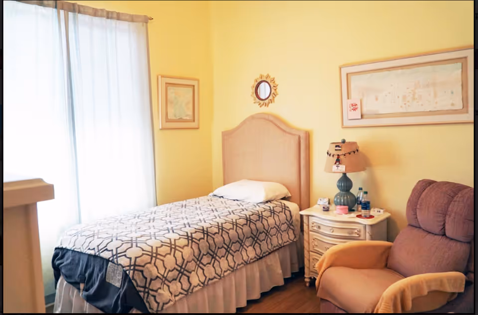 A cozy yellow bedroom featuring a single bed, nightstand, lamp, and armchair.