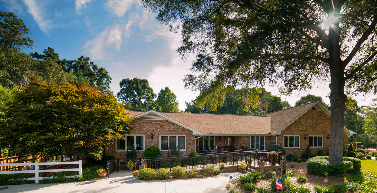 Single-story brick senior living facility with manicured landscaping and a large tree in front.