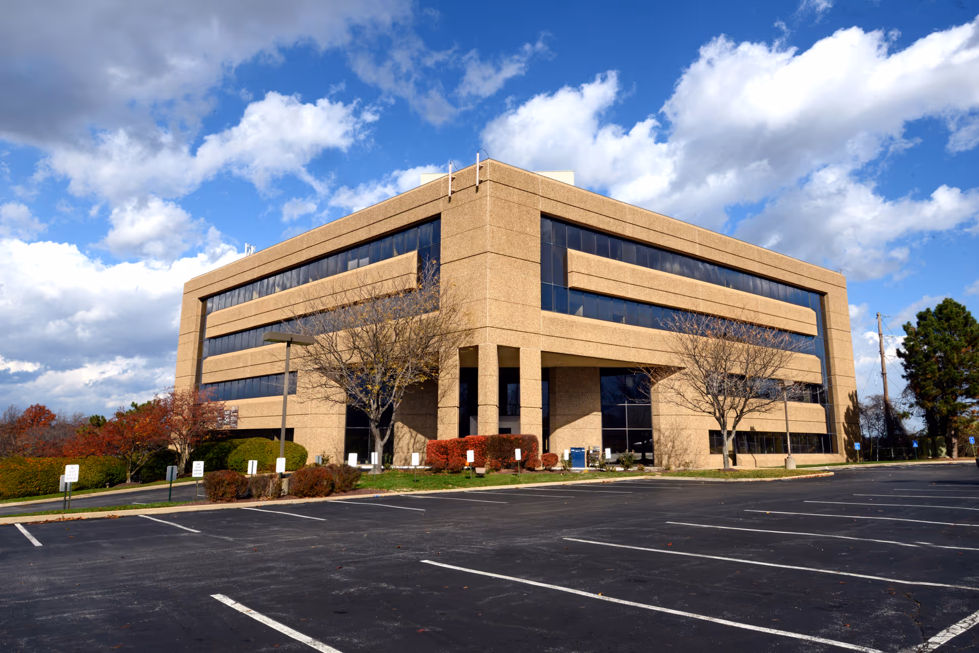 A large beige brick office-style building with a parking lot and blue sky