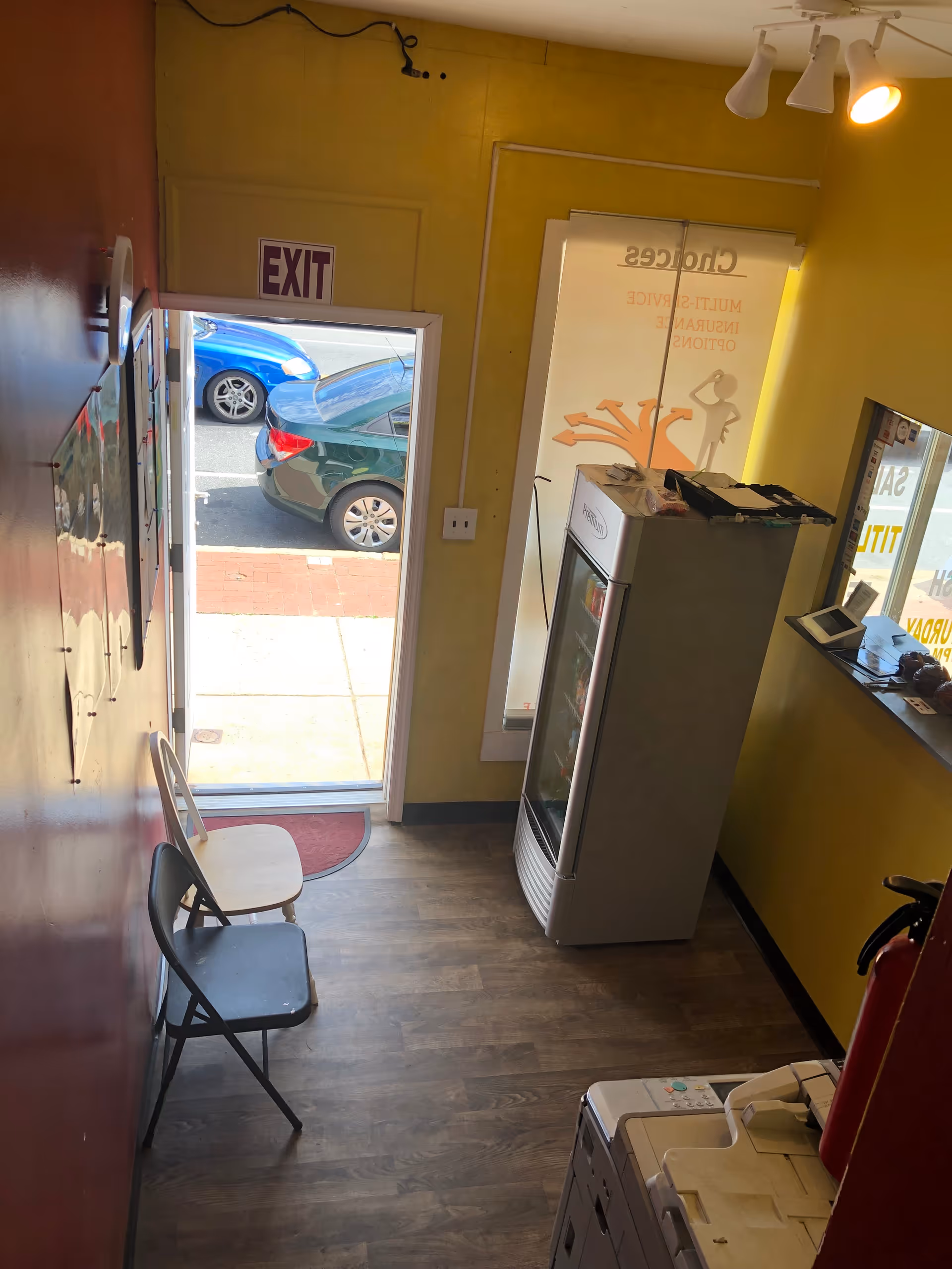 Narrow hallway lobby with chairs, a vending cooler, and an exit door to outside.
