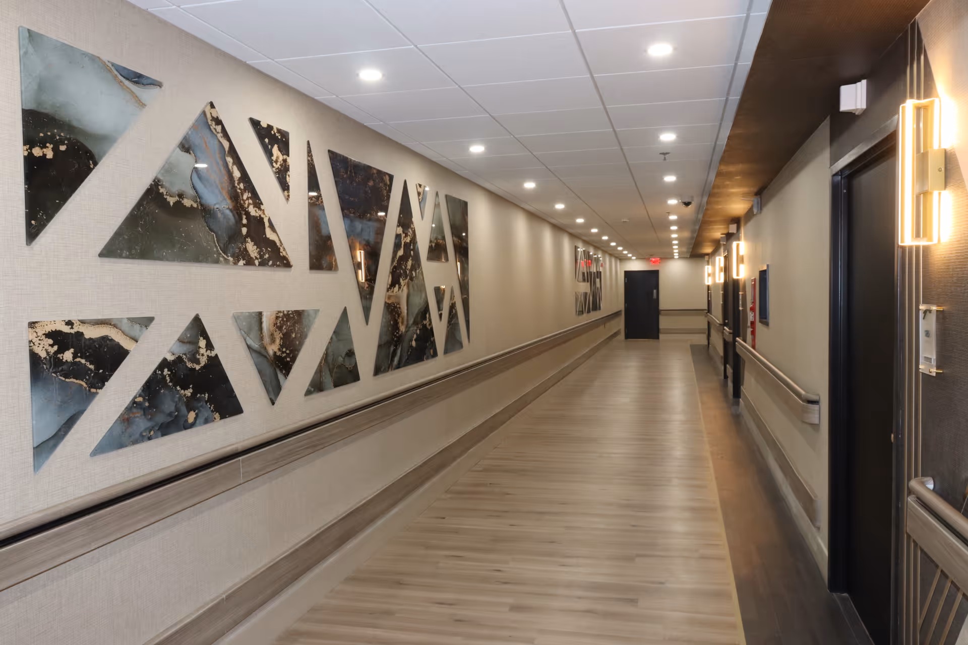 Long interior hallway with abstract wall art and overhead lighting in a senior facility.