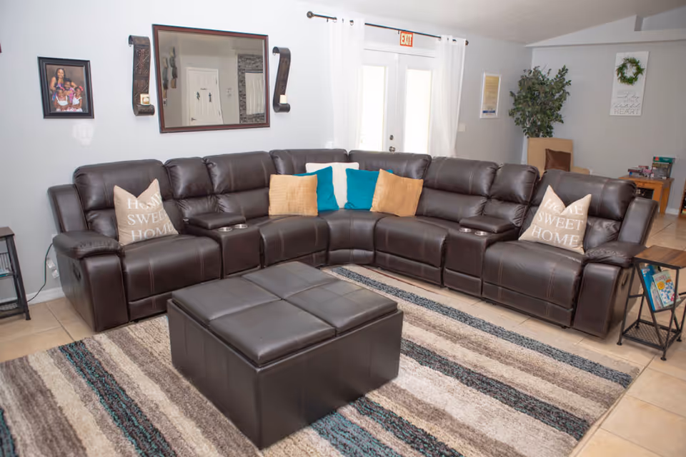 A spacious living room with a brown leather sectional, ottoman, and decorative pillows.
