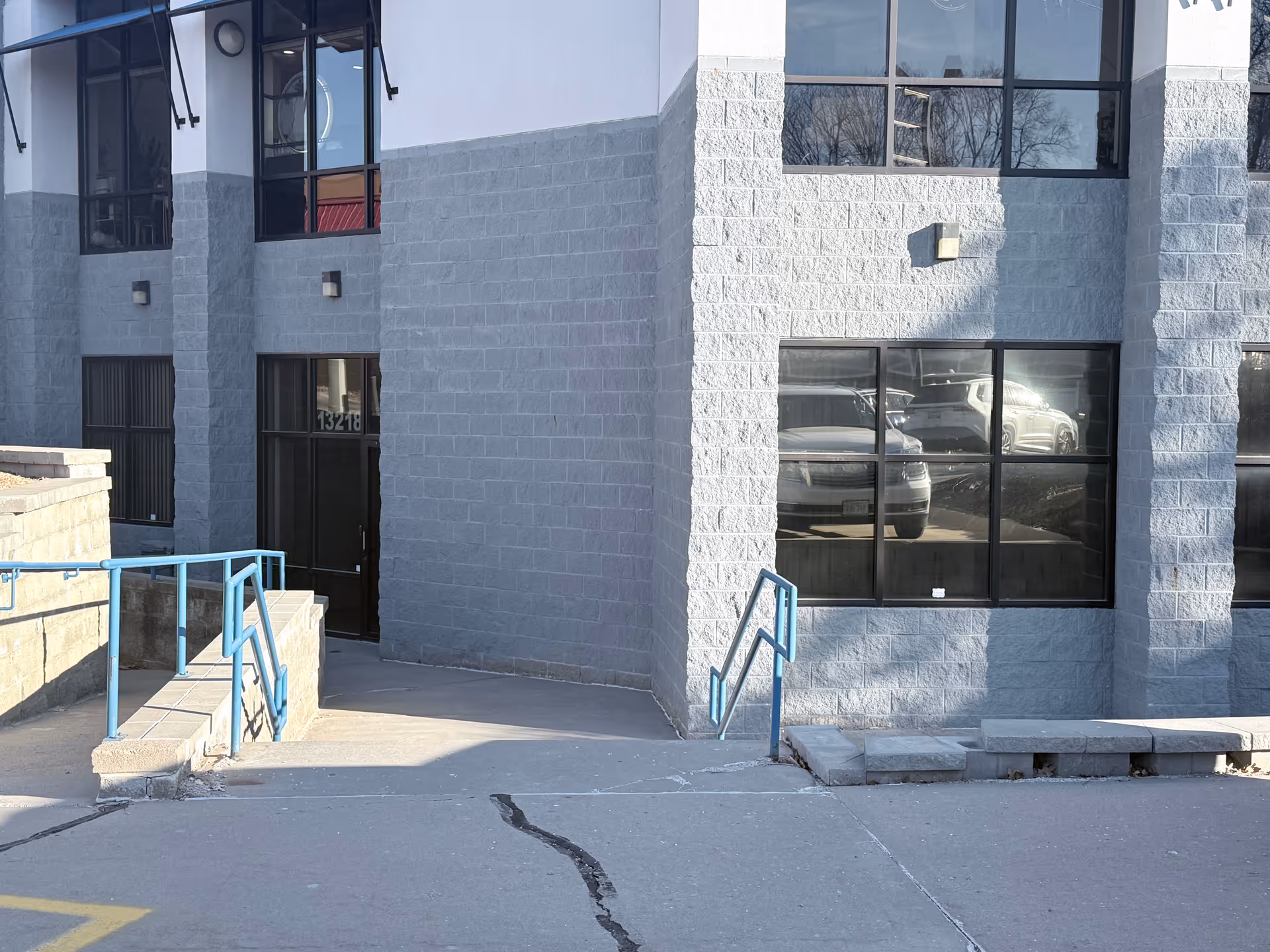 Blue-gray exterior of a commercial building with stairs, handrails, and large glass windows.