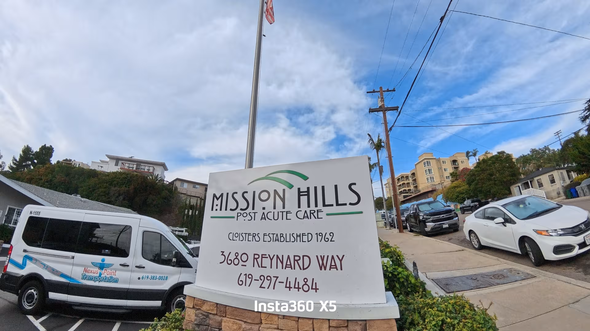 Exterior view of Mission Hills Post Acute Care sign beside parked vans on a street.