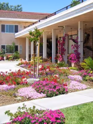 Exterior view of The Californian facility with colorful flower beds and a shaded walkway.