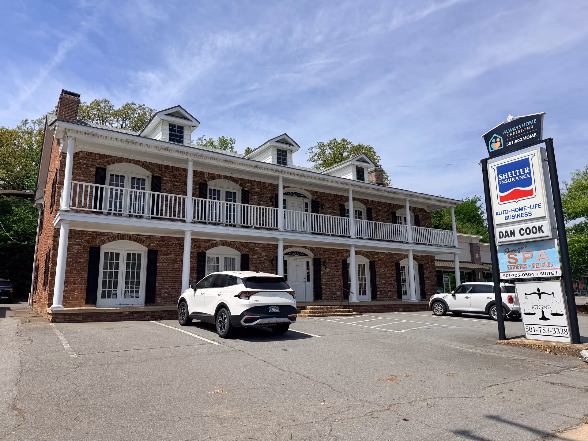 Exterior view of a brick two-story facility with white columns and parked cars.