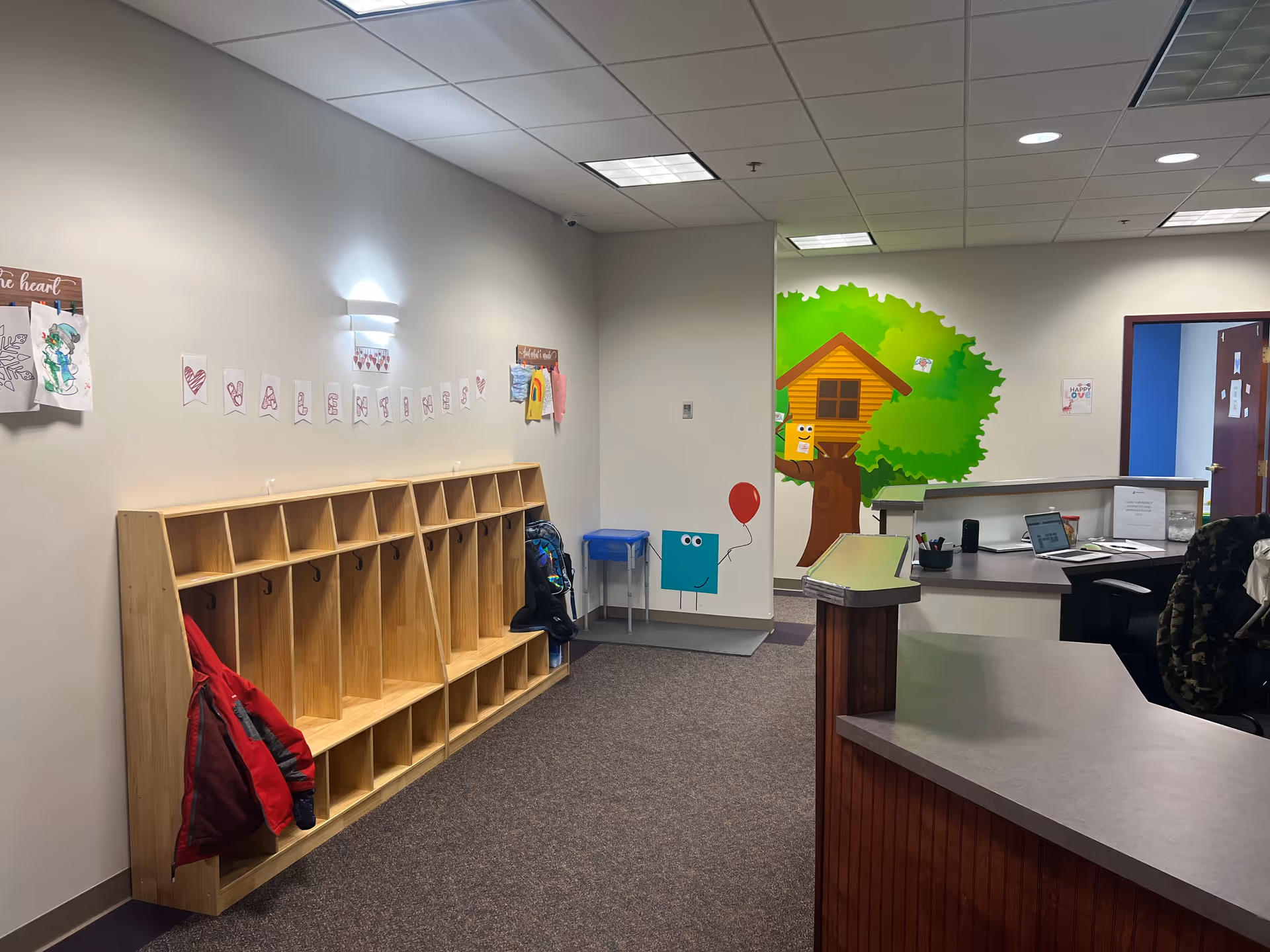 Reception desk and cubbies along wall with colorful mural in a clinic lobby.