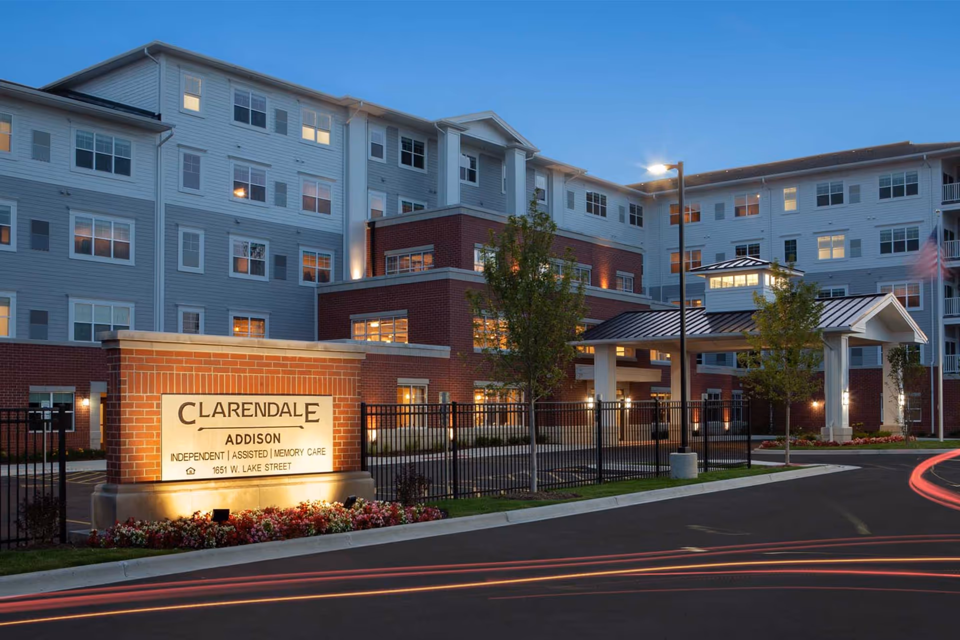 Exterior view of Clarendale Addison senior living facility with brick sign and entrance.
