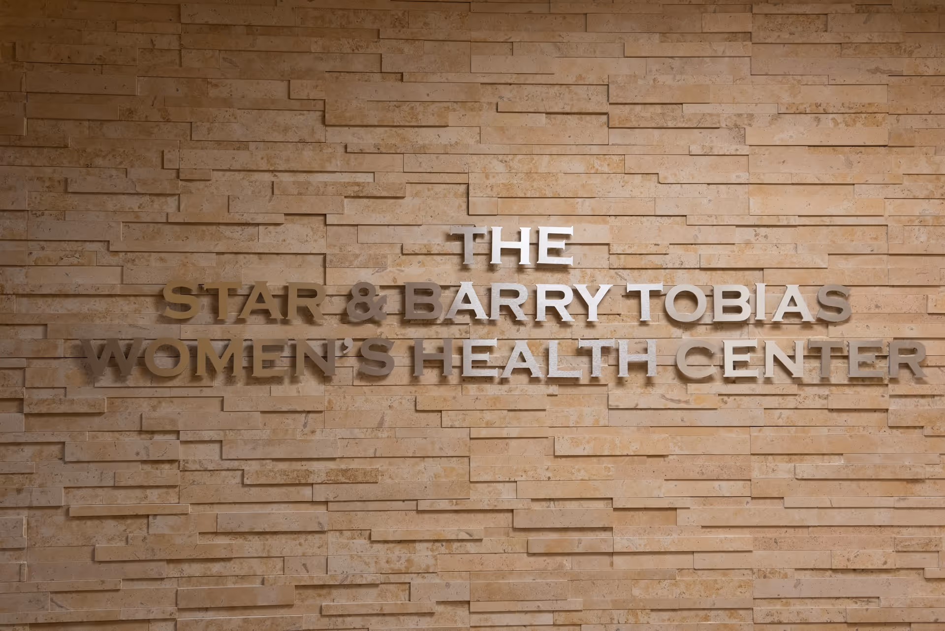 Stone wall with bold metal letters reading The Star & Barry Tobias Women's Health Center.