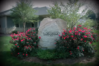 A stone sign reading WillowBrook Memory Care surrounded by pink roses.