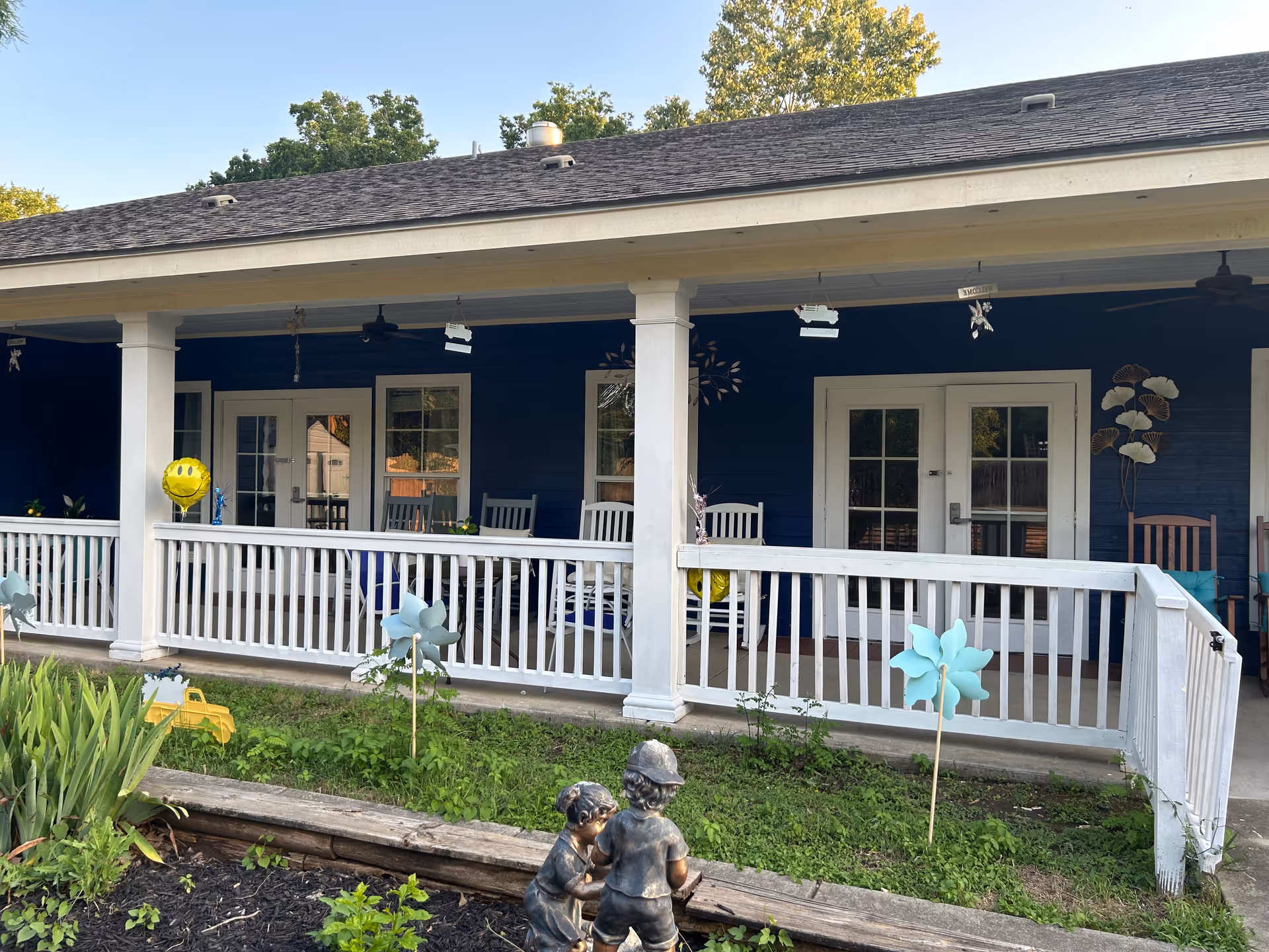 Blue exterior porch of a senior living facility with white railings and rocking chairs.