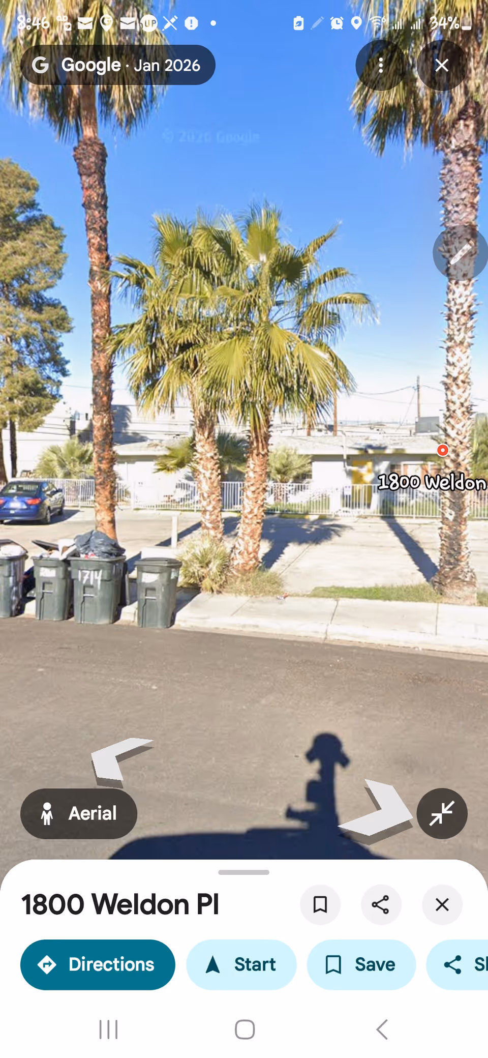 Street view of a senior living facility exterior with palm trees and parked bins.