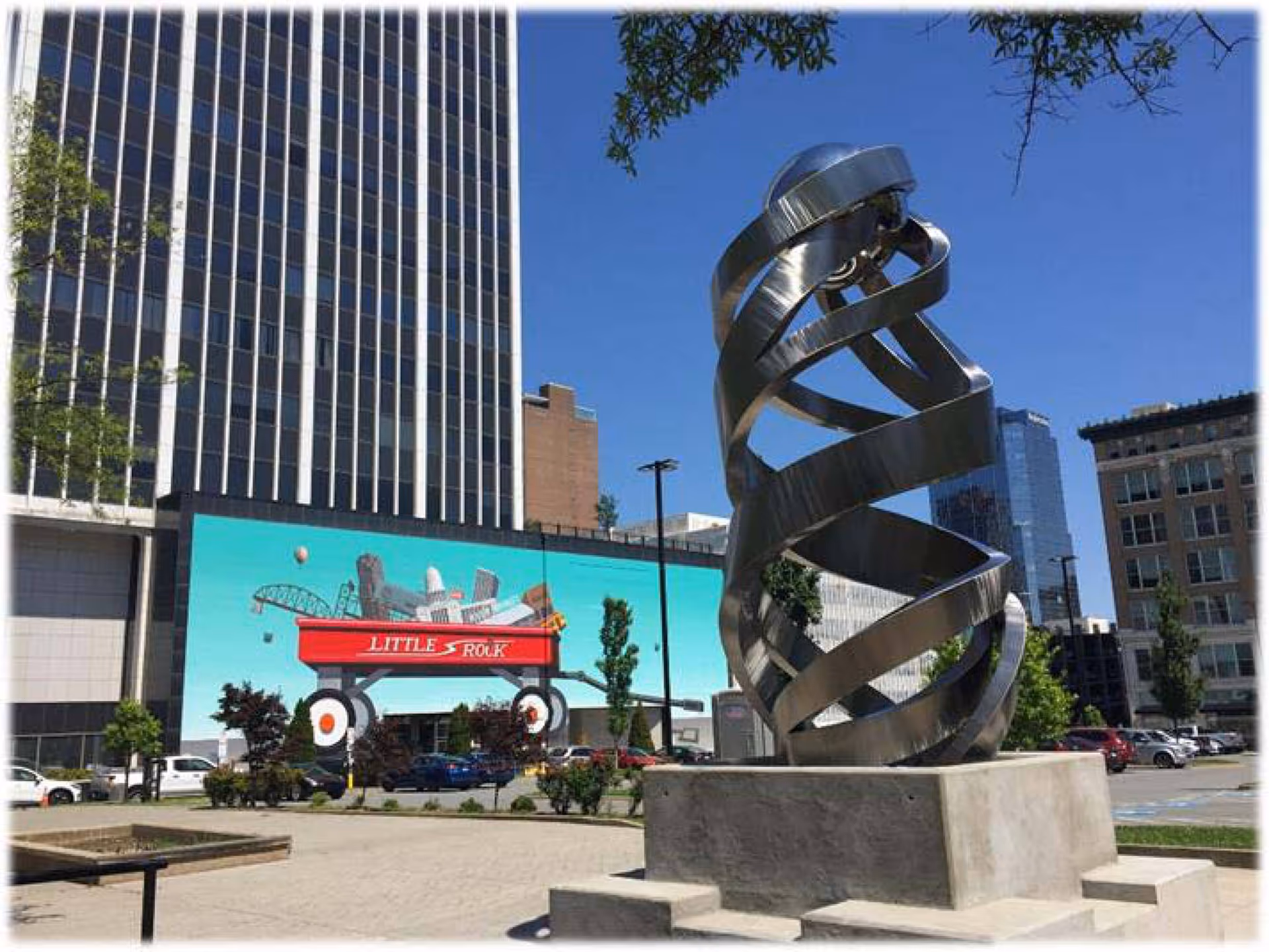 Urban outdoor plaza with a spiraling metal sculpture and a mural on the building.