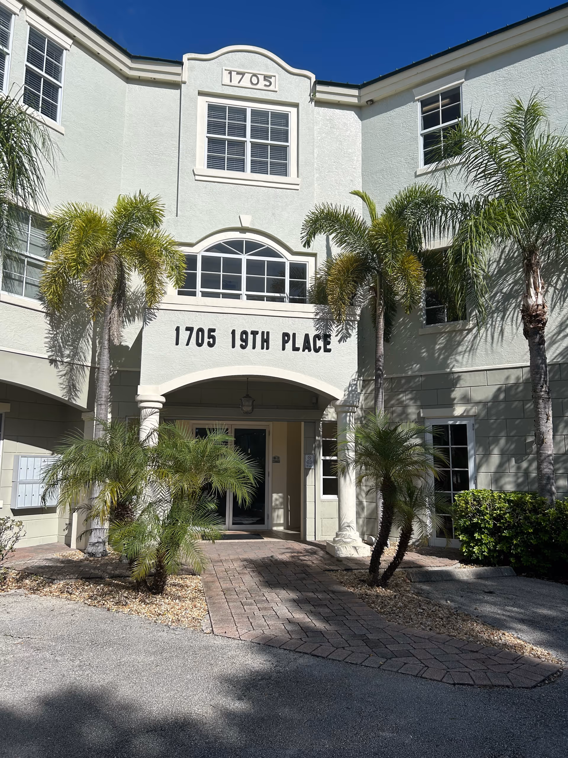 Light-colored two-story building entrance with palm trees and the address 1705 19th Place.
