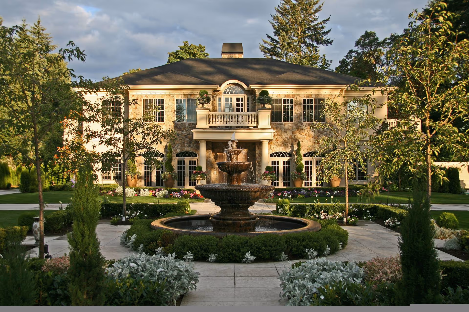 Stone two-story building with a central tiered fountain and formal landscaped garden in front.
