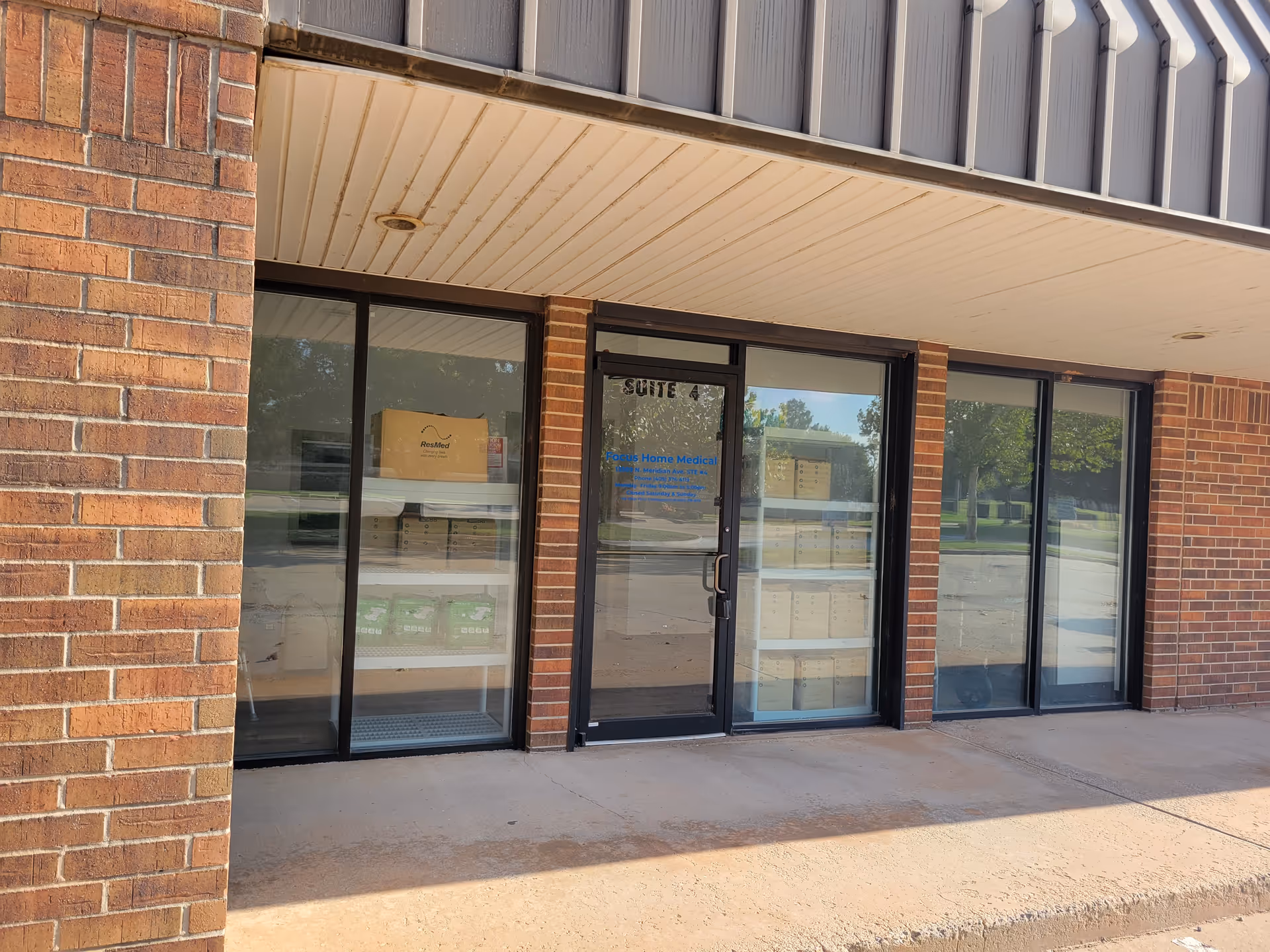 Brick storefront with glass doors and windows showing boxed supplies inside