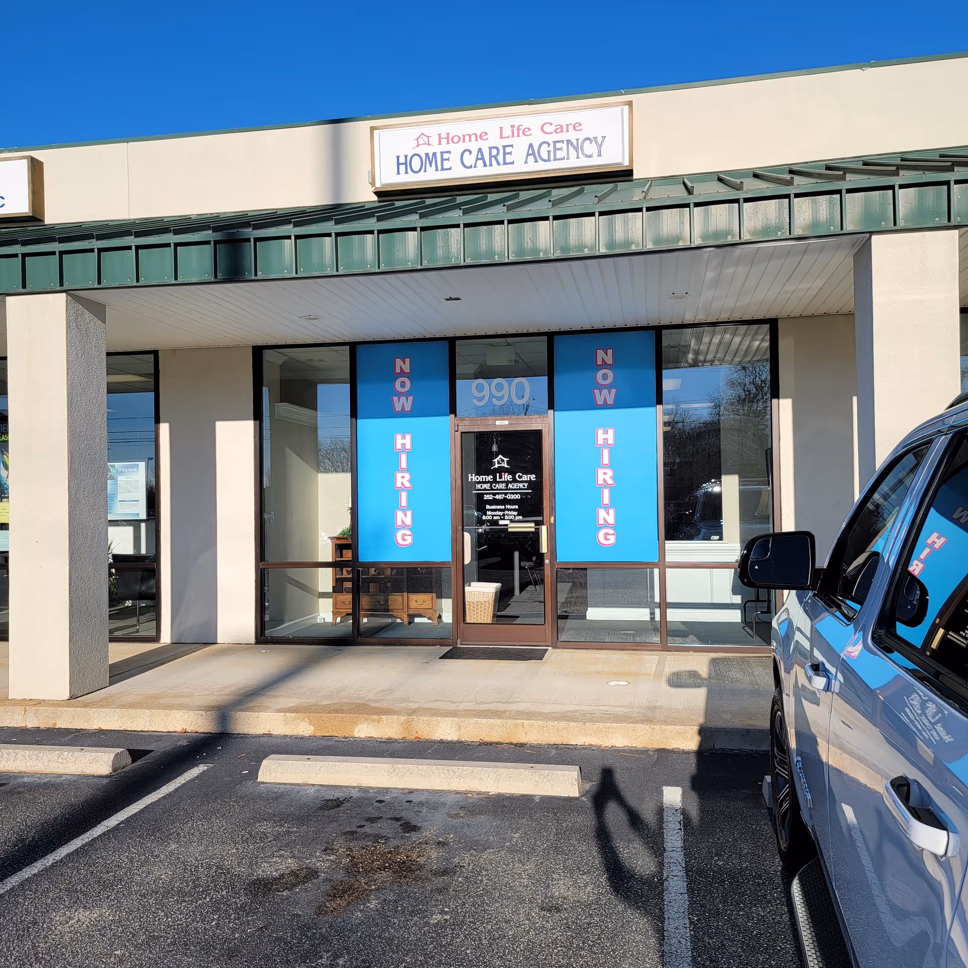 Exterior view of Home Life Care Agency storefront with blue hiring banners and a parked vehicle.