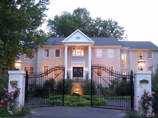 Gated entrance to Great Falls Manor, a stone building with lampposts.