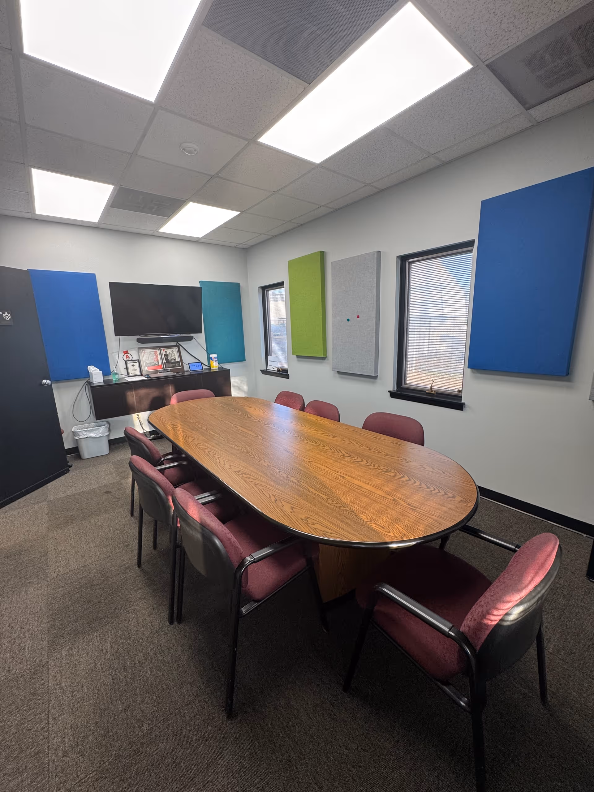 An oval wooden conference table with maroon chairs in a furnished meeting room.
