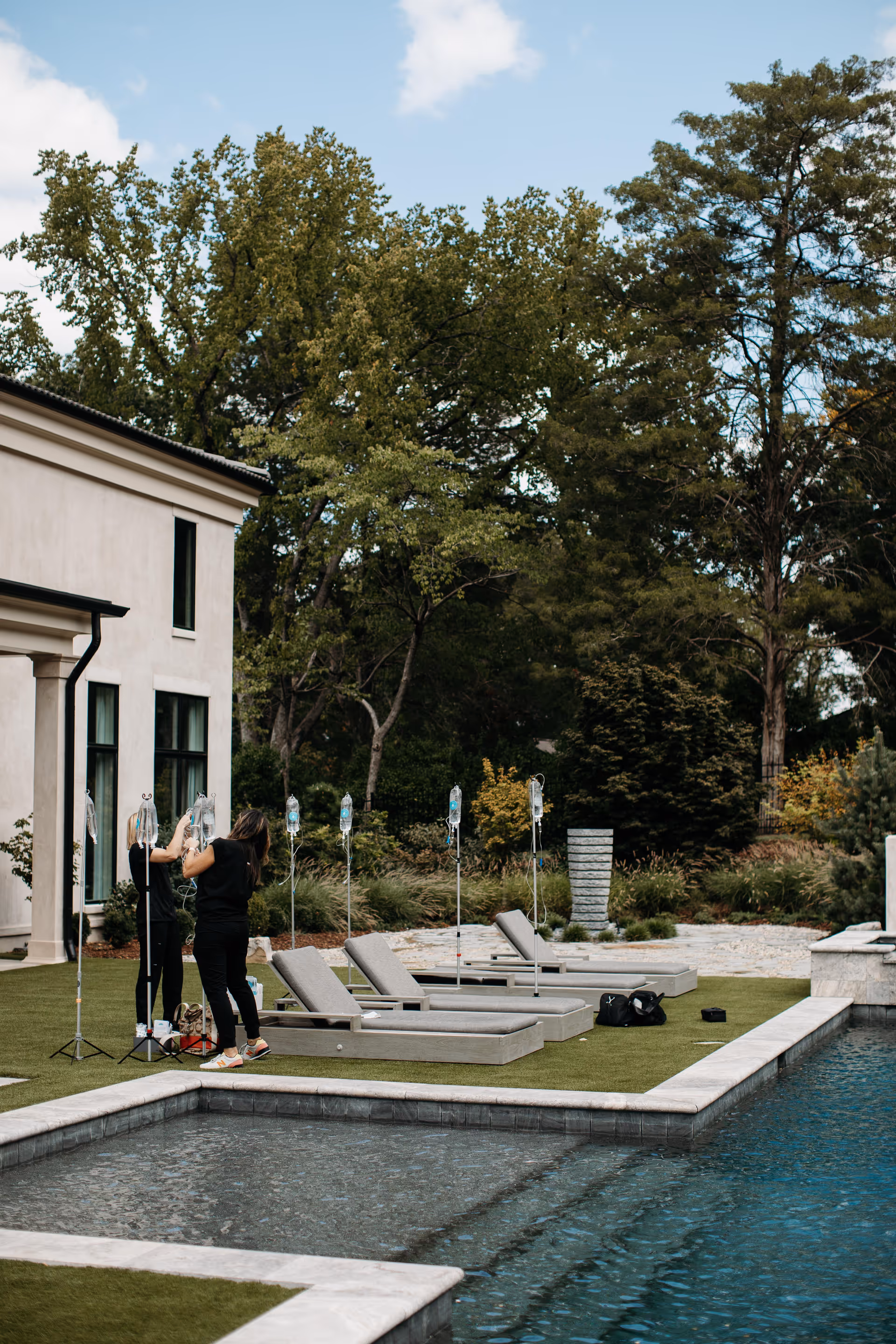 Outdoor poolside area with lounge chairs and a person adjusting IV equipment near the building.