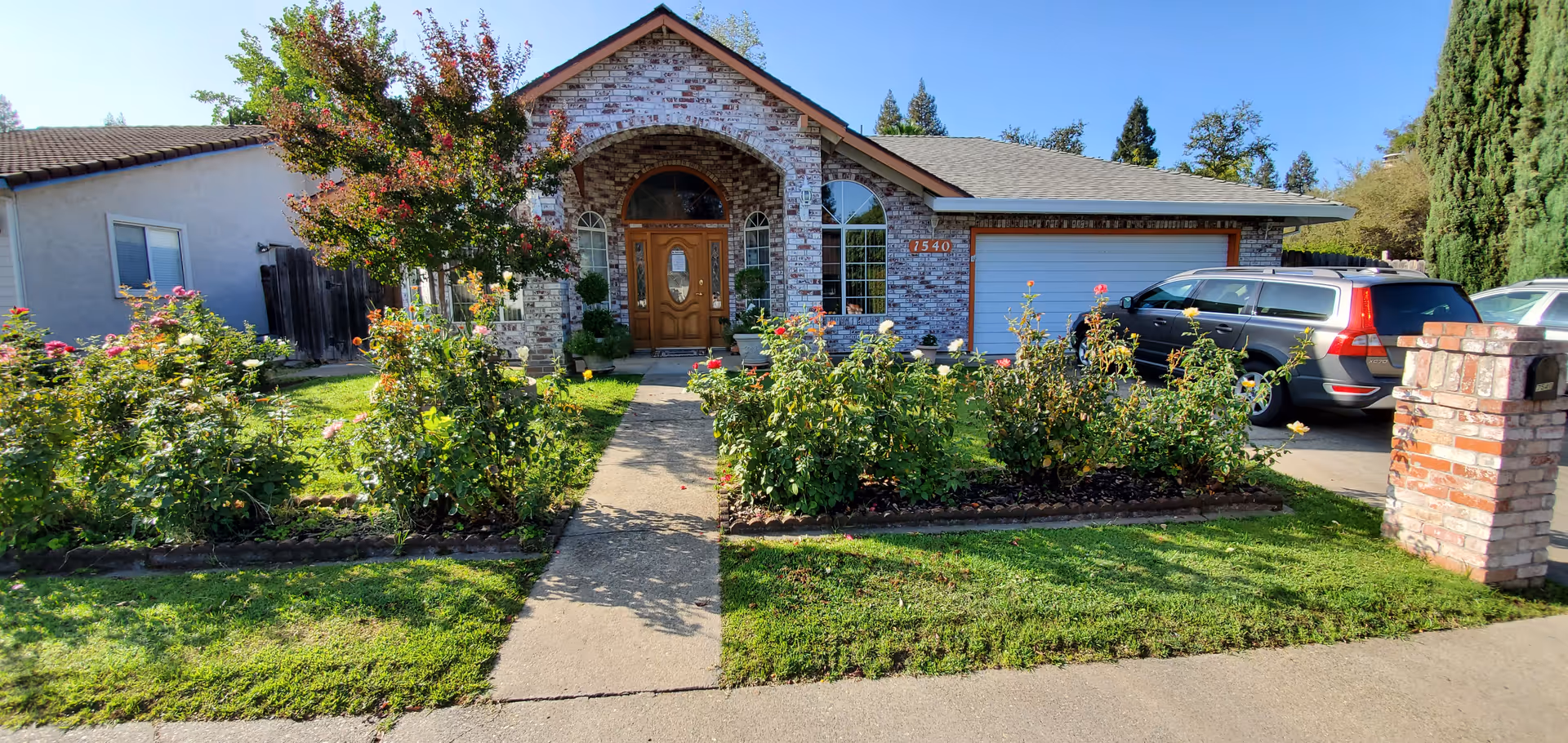 Front view of a brick house with a garden and parked cars.