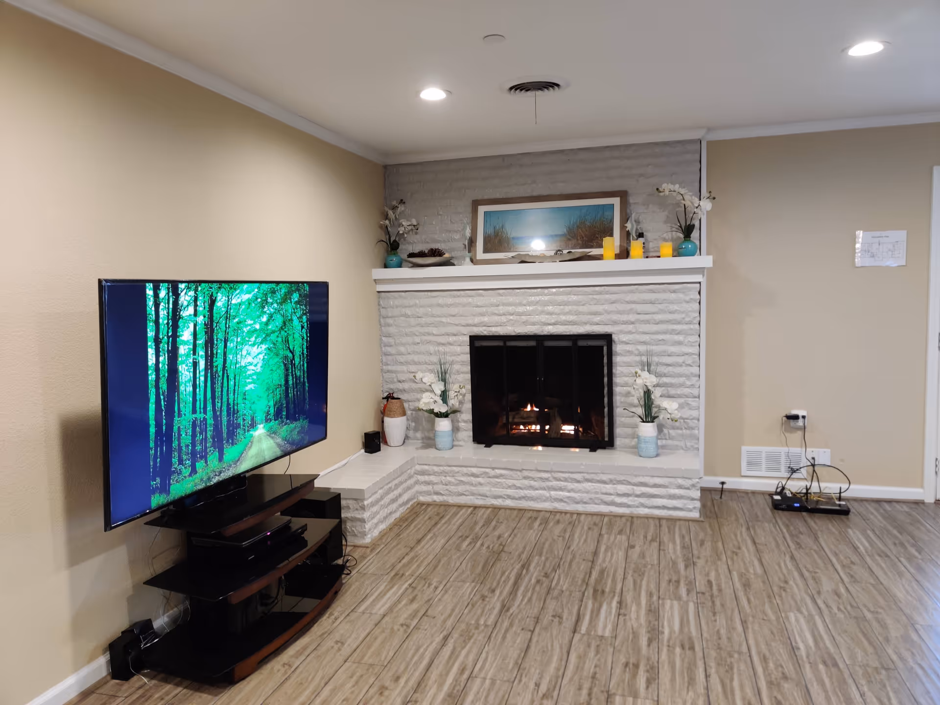 Cozy living room with a white brick fireplace, TV, and decorative mantle along beige walls.