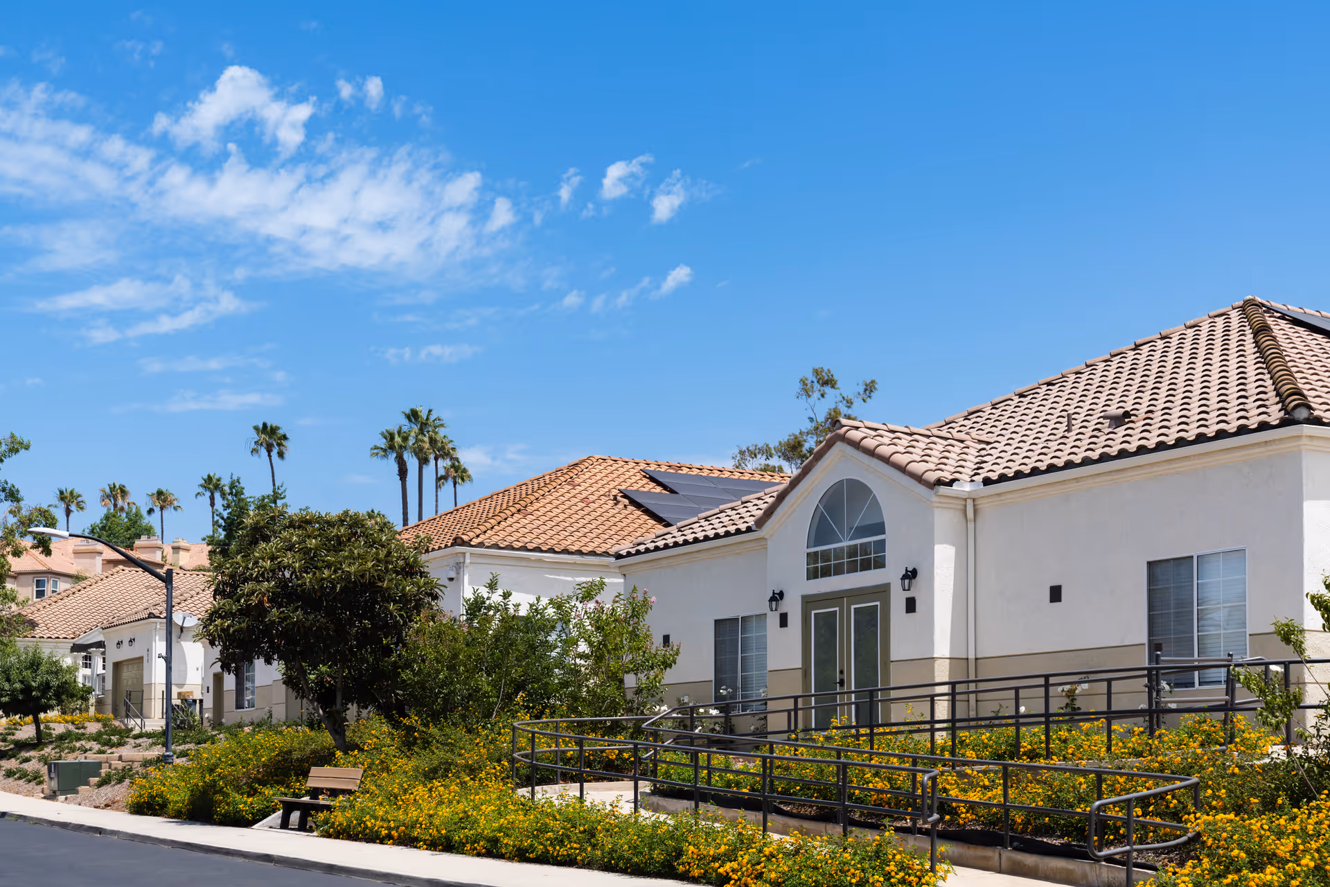 Exterior view of Oak Hill Residential Care facility with beige stucco walls, tiled roof, and landscaping.