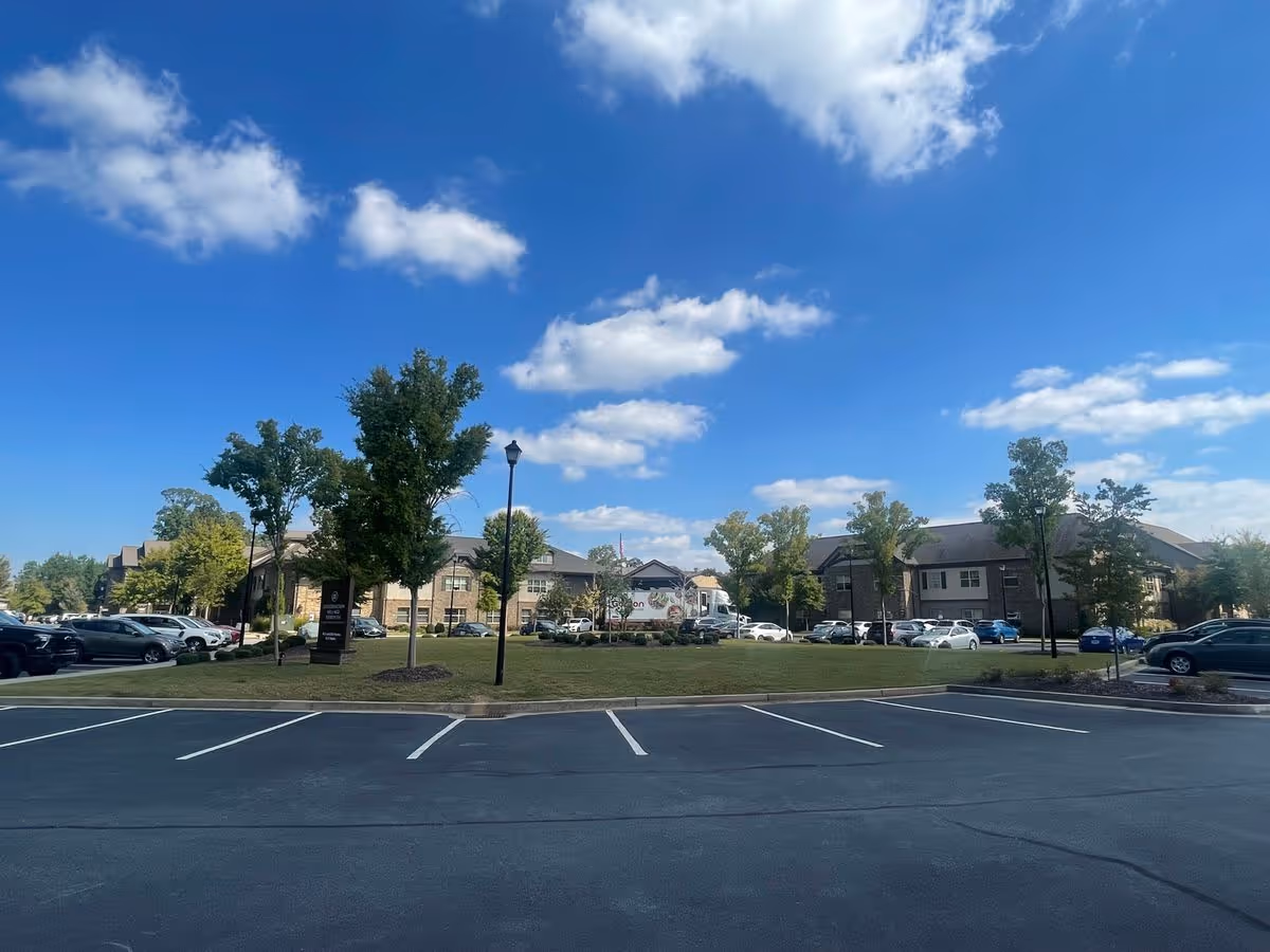 Front view of Celebration Village Forsyth with a parking lot, lawn and trees under a blue sky with scattered clouds.