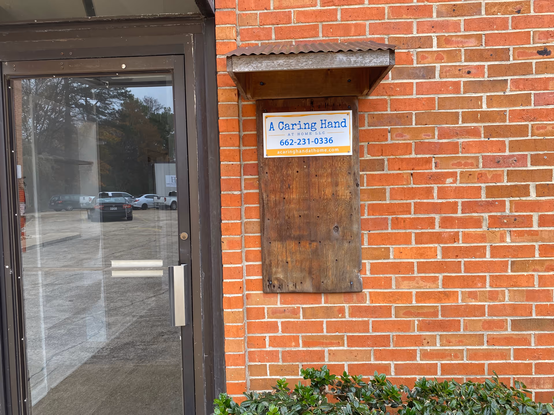 Brick exterior with glass entry door and a wooden sign for A Caring Hand at Home.