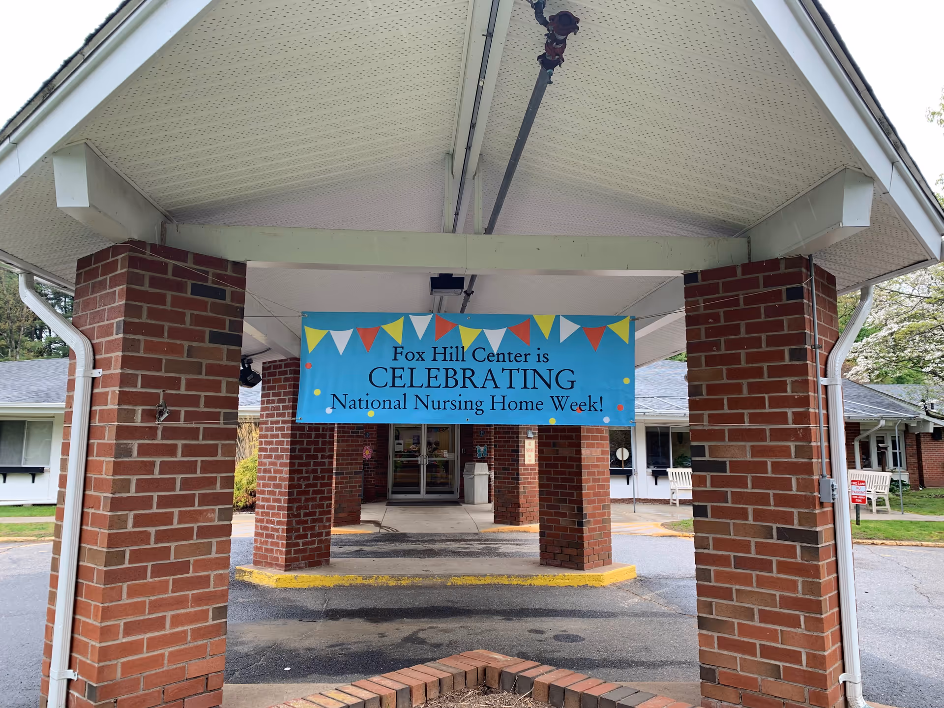 Brick entrance canopy with banner celebrating National Nursing Home Week at Fox Hill.