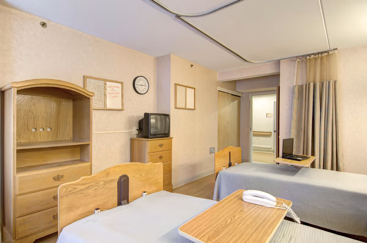 Two single hospital beds with light wood furniture and a TV in a patient room.