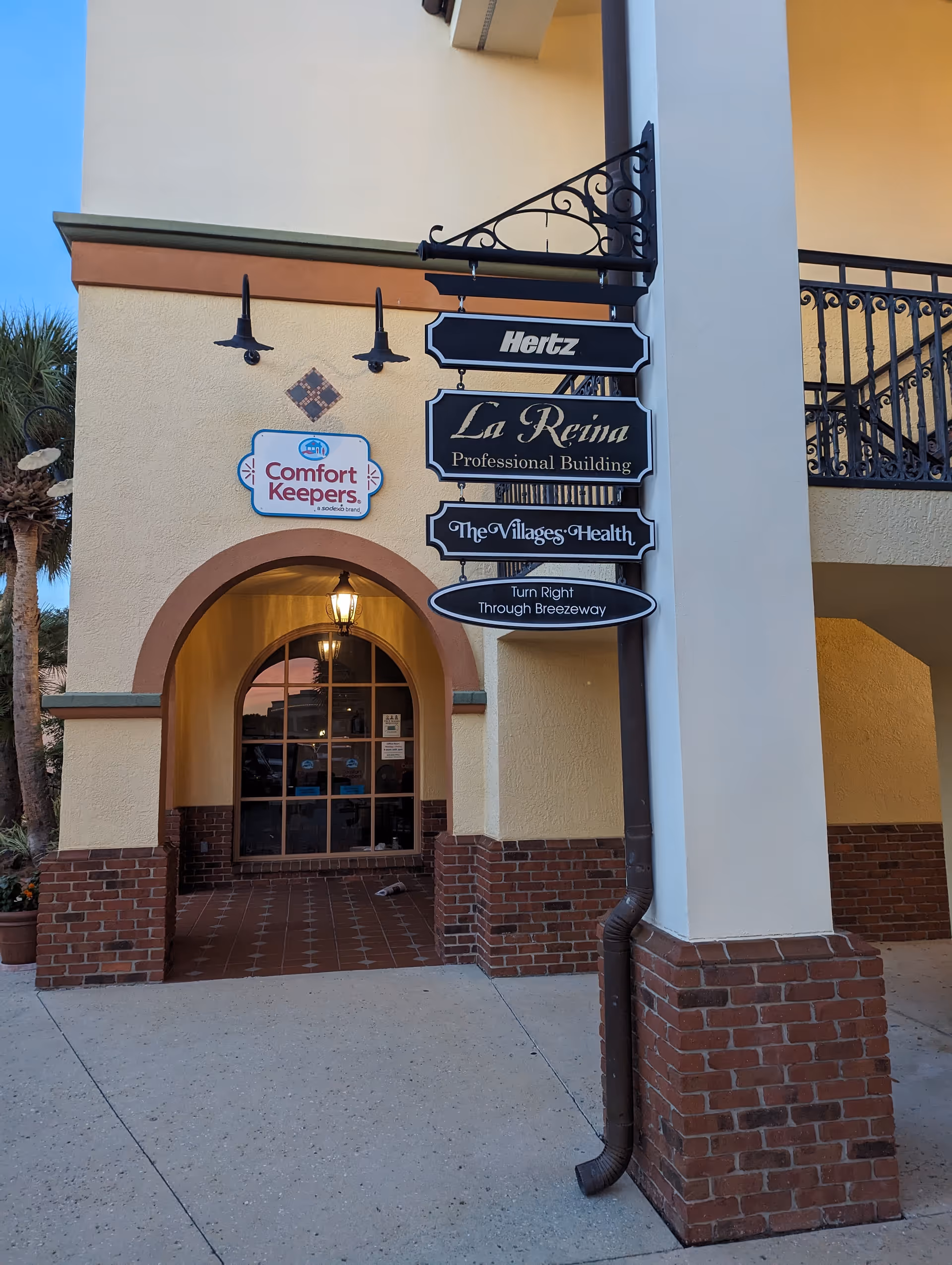 Exterior building entrance with arched doorway and multiple signs, including Comfort Keepers logo.