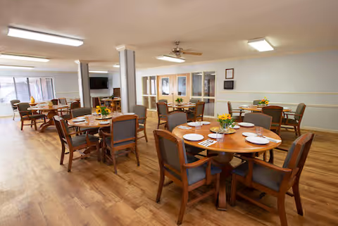 Bright dining room at Autumn Care of Raeford with round tables, chairs, and flowers.