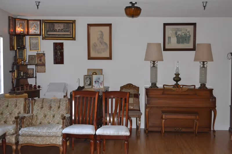 A vintage-style living room with chairs, a sofa, a piano, lamps, wall pictures, and wood floor.