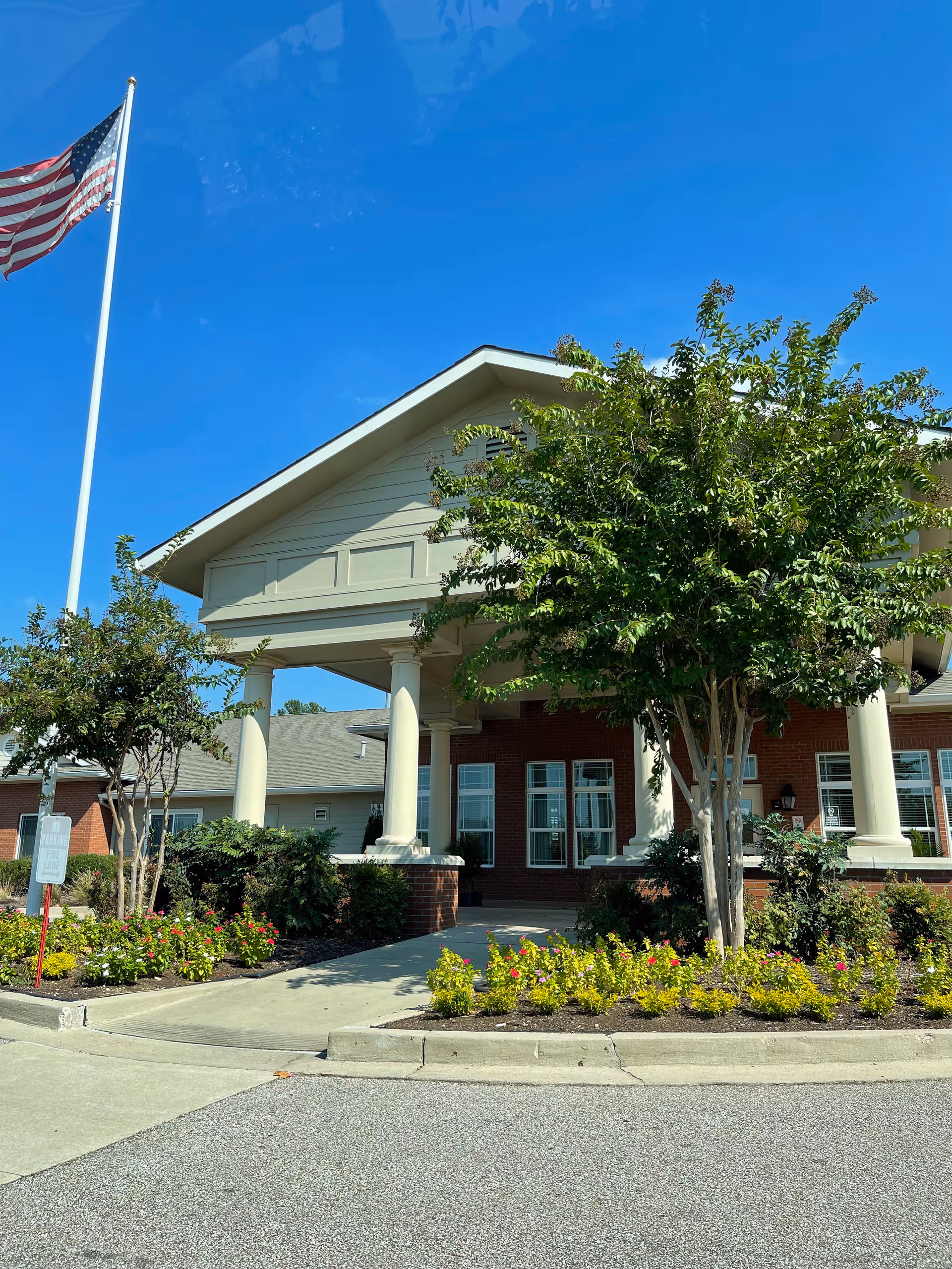 Front entrance of Quail Ridge Assisted Living and Memory Care building with flag and landscaping.