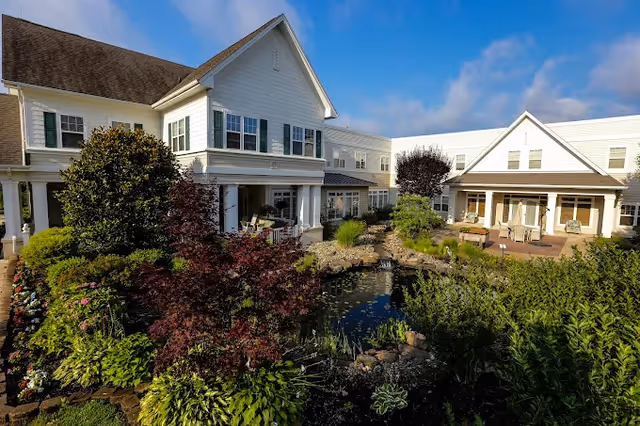 Cream-colored senior living building surrounding a landscaped garden pond with outdoor seating.