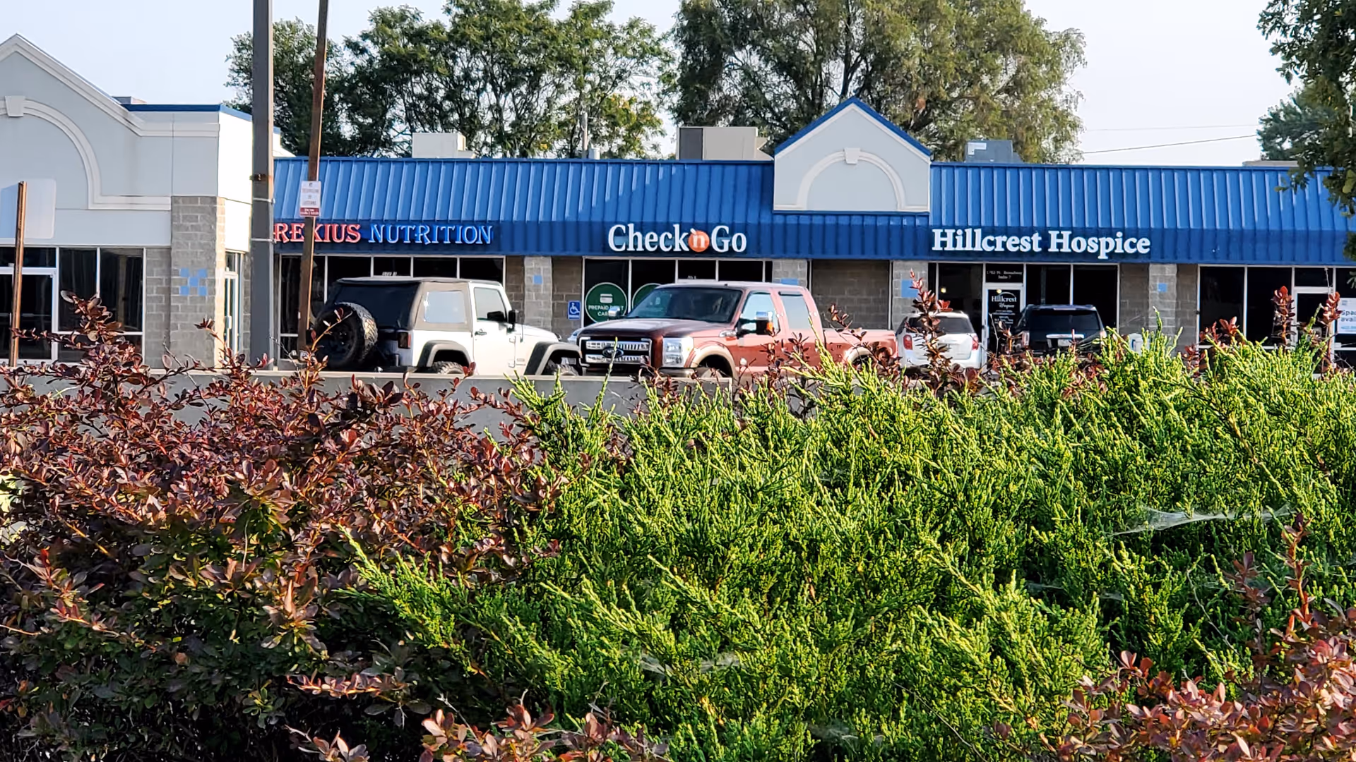 Exterior view of a strip mall with Hillcrest Hospice sign and cars in the parking lot.