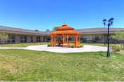 Orange gazebo sits in a grassy courtyard with a single-story building in the background.