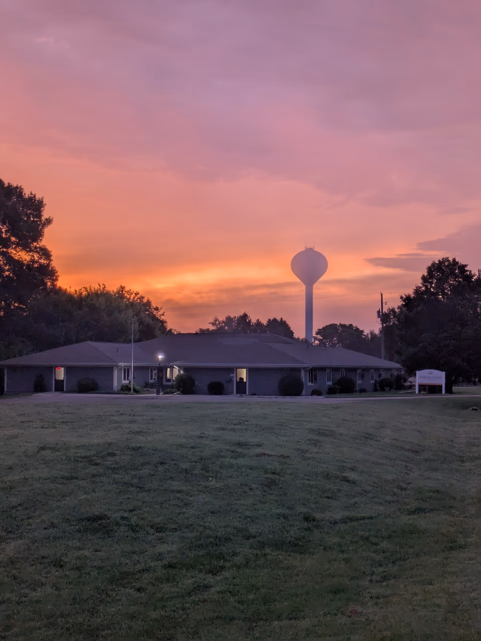 Sunset sky over a single-story senior living building with a tall water tower in distance.