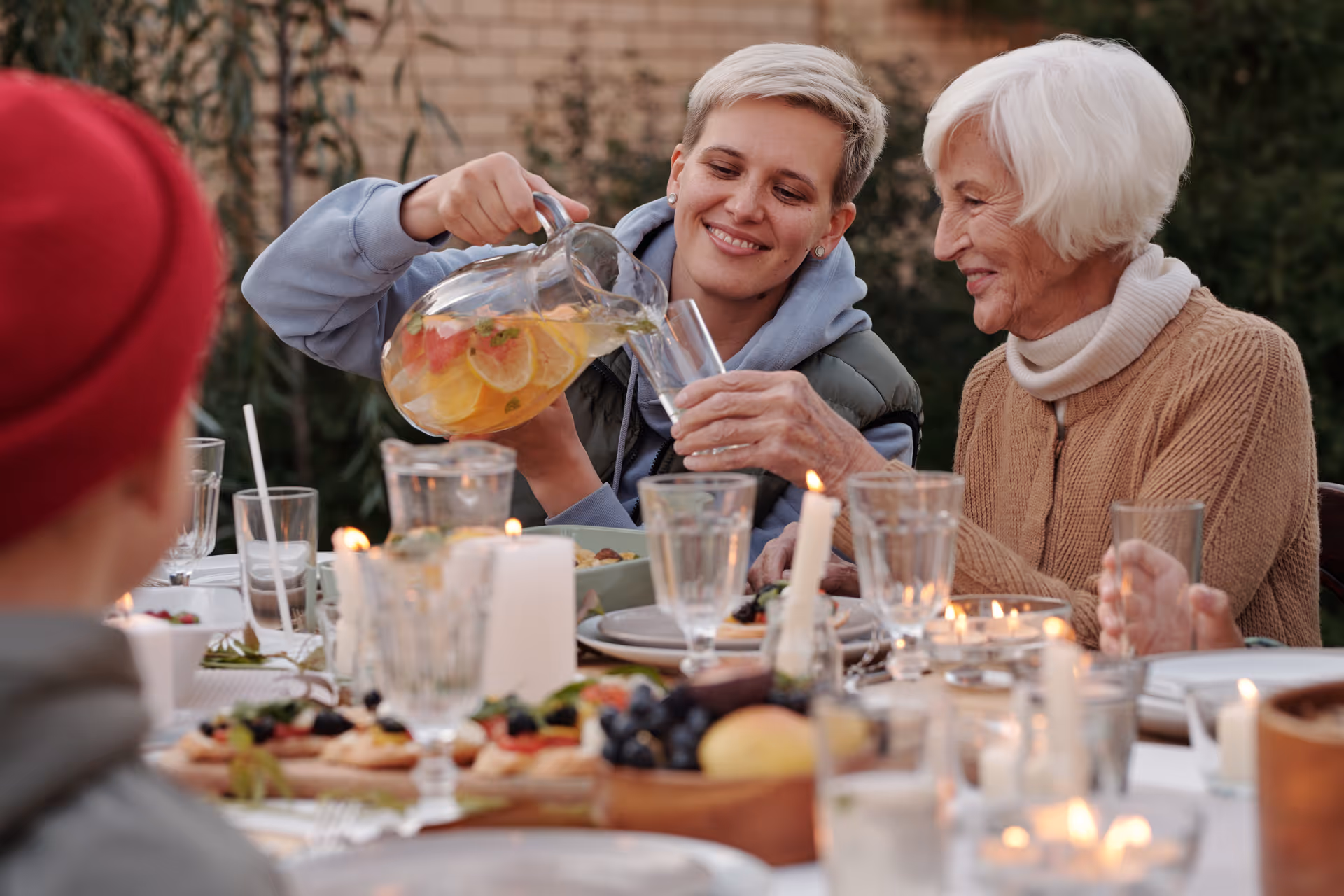 Two residents dining outdoors at a candlelit table, pouring drinks and sharing a meal.