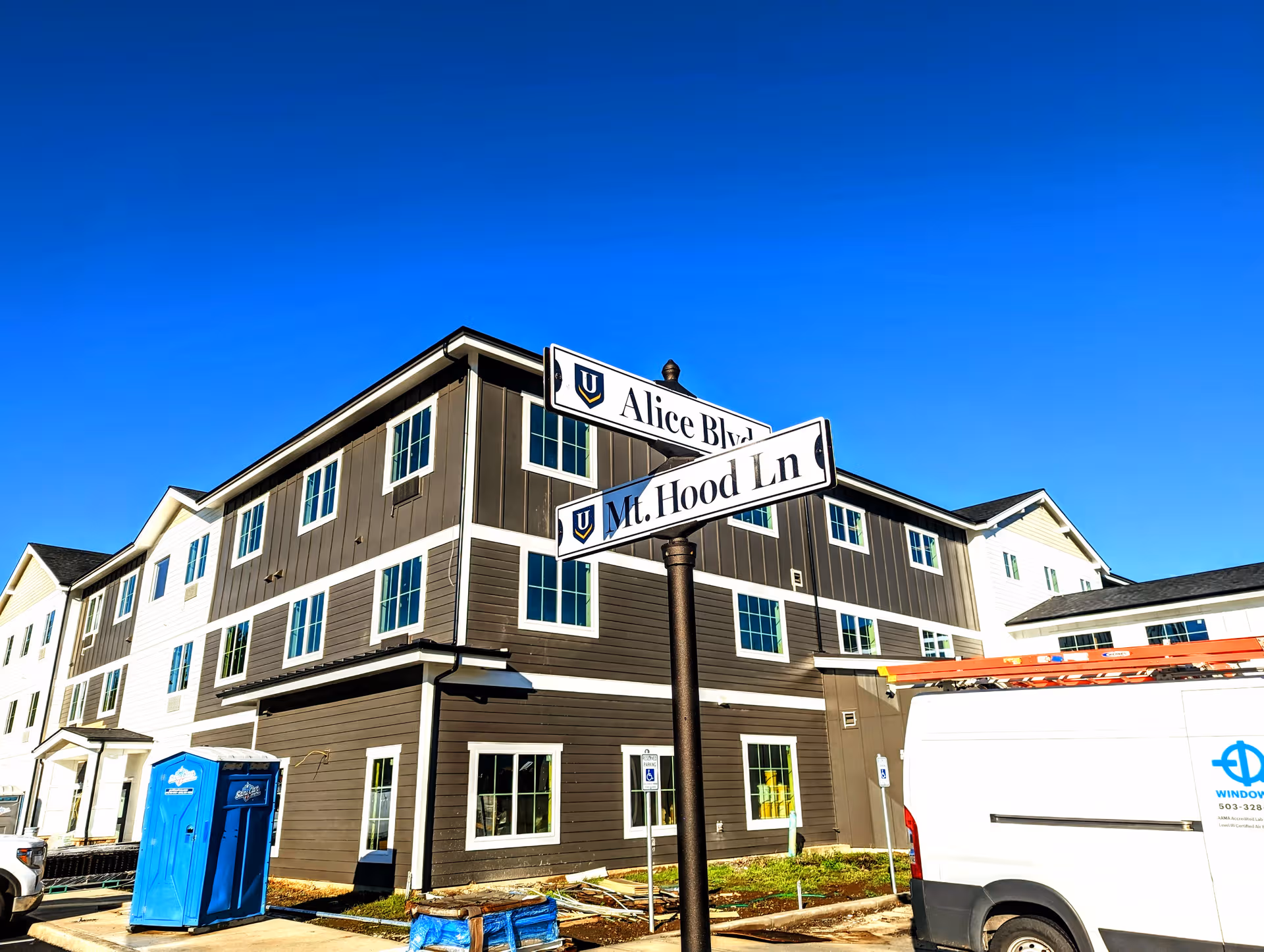Exterior view of a brown, multi-story senior living building with street signs and a portable toilet.