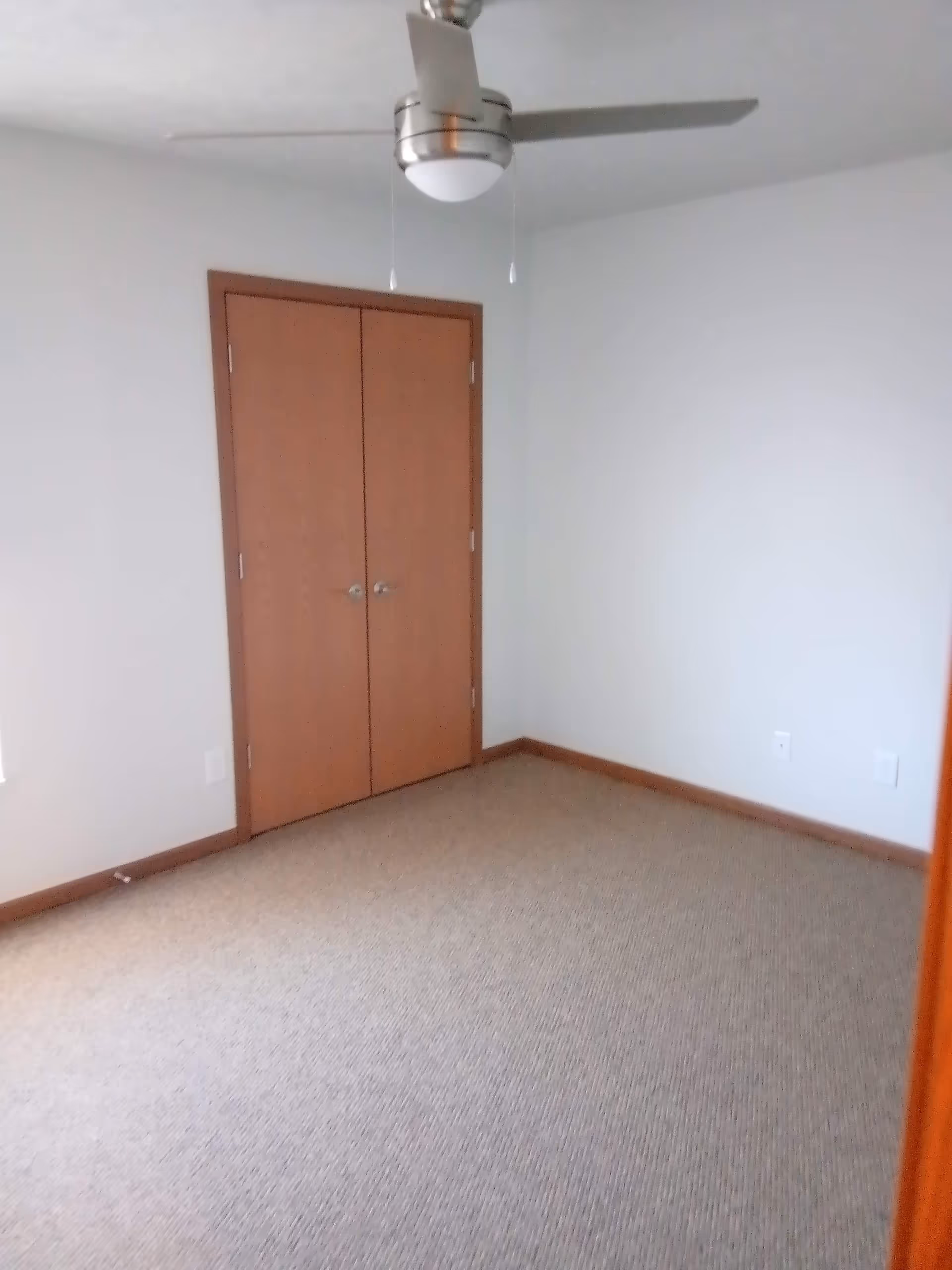 Empty beige carpeted room with double closet doors and a ceiling fan.