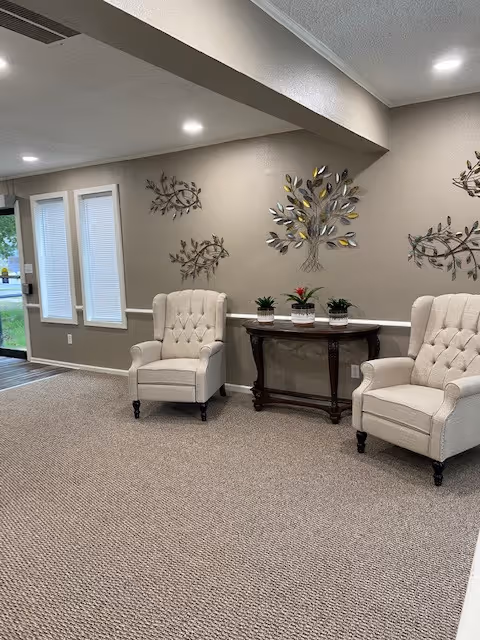 Two beige tufted armchairs flank a wooden console table with potted plants in a lounge.
