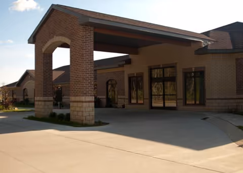 Brick senior living facility entrance with a covered drop-off area and glass doors.