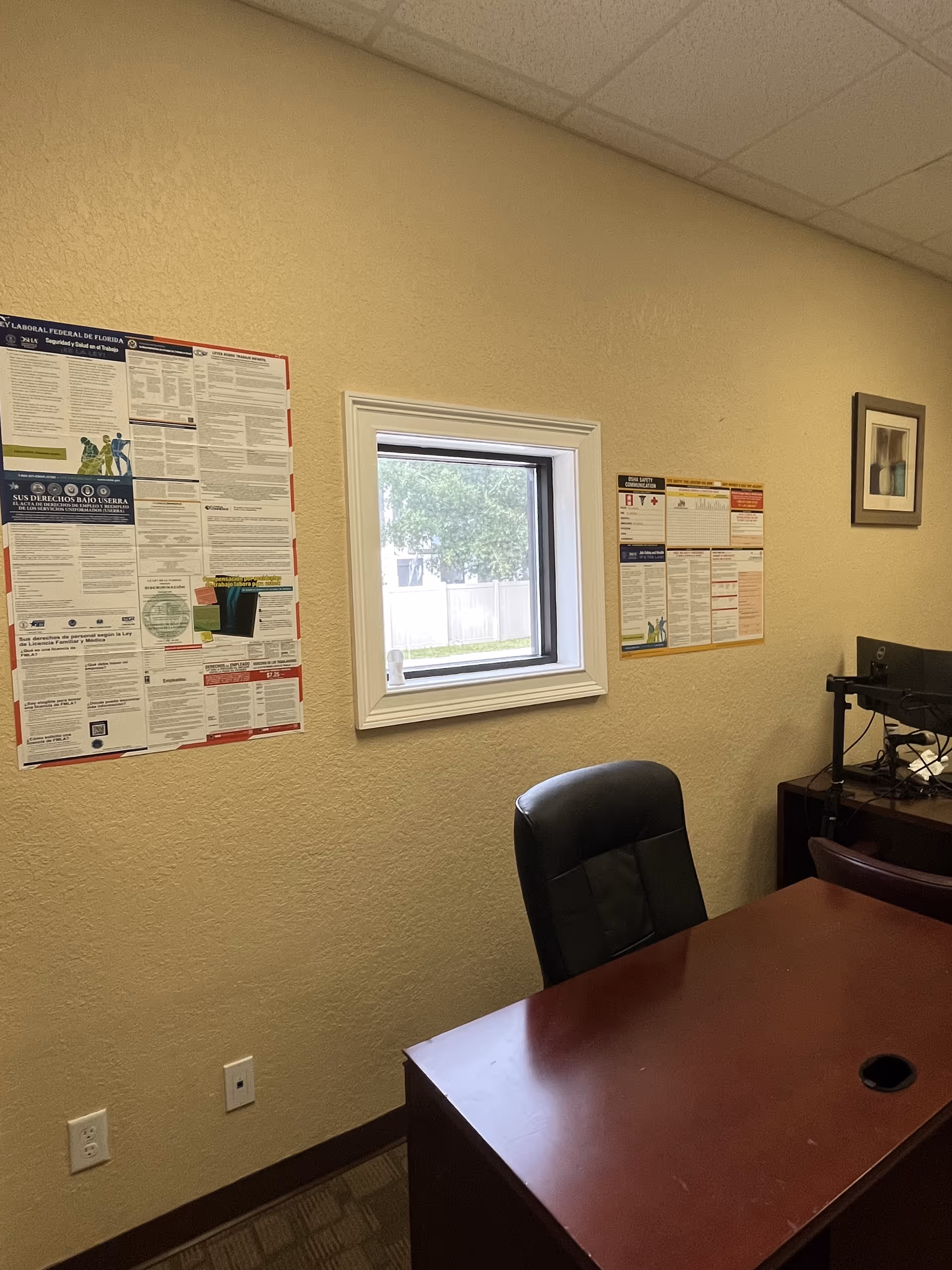 Office desk and chair in a beige room with wall posters and a window.