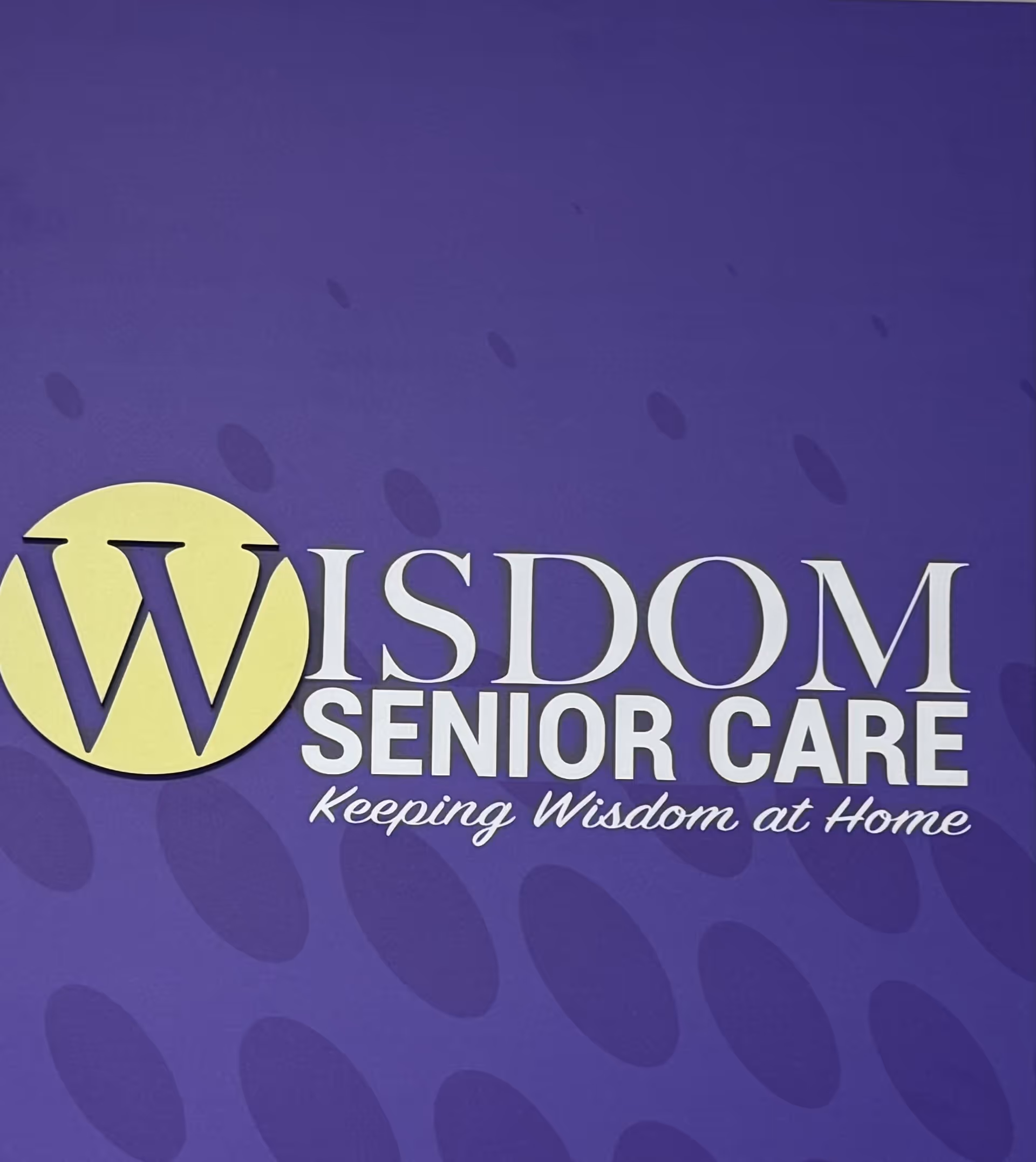 Purple wall sign featuring Wisdom Senior Care logo and slogan Keeping Wisdom at Home.