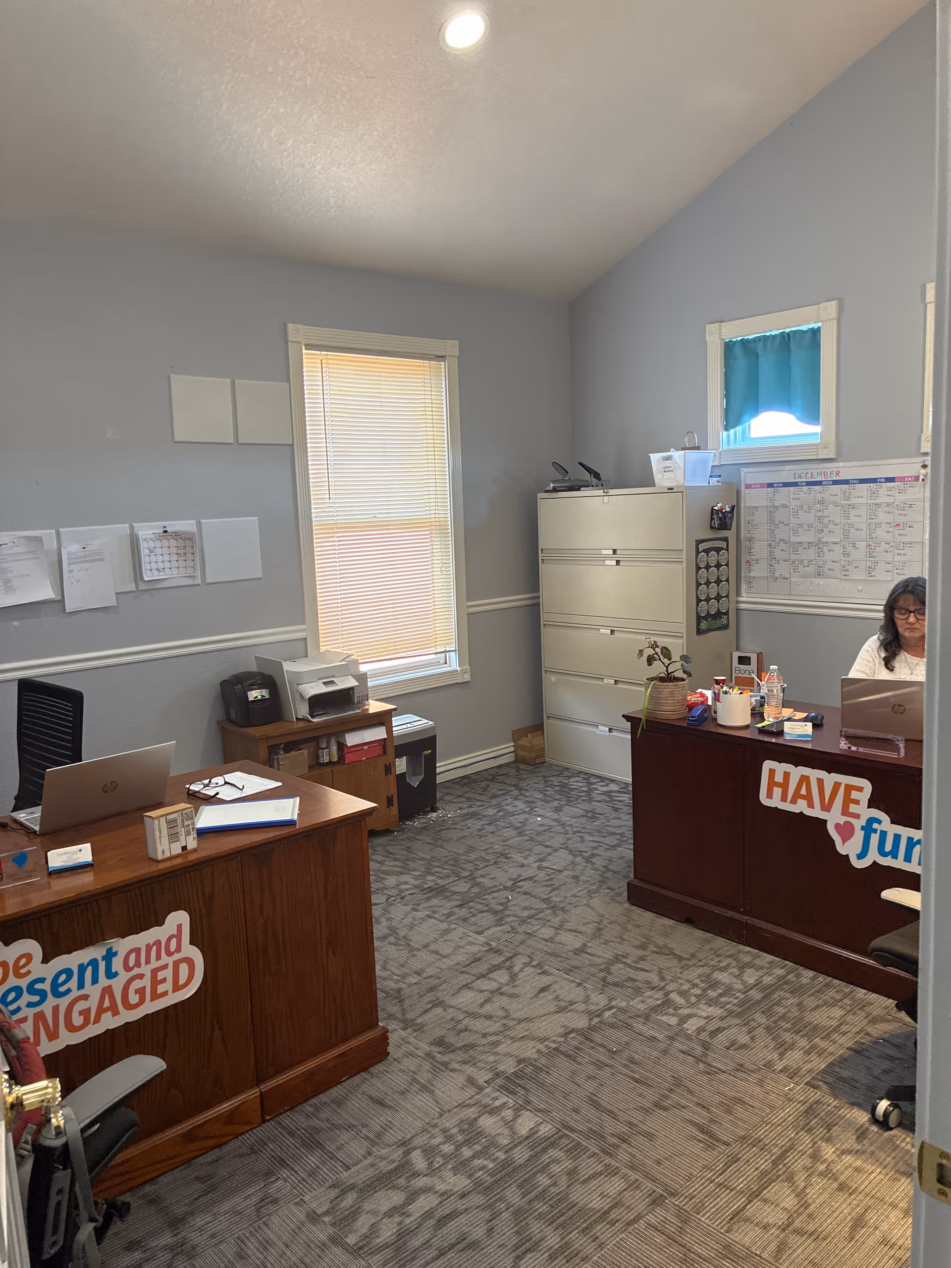 A small office/reception area with two desks, filing cabinets, and a staff member.