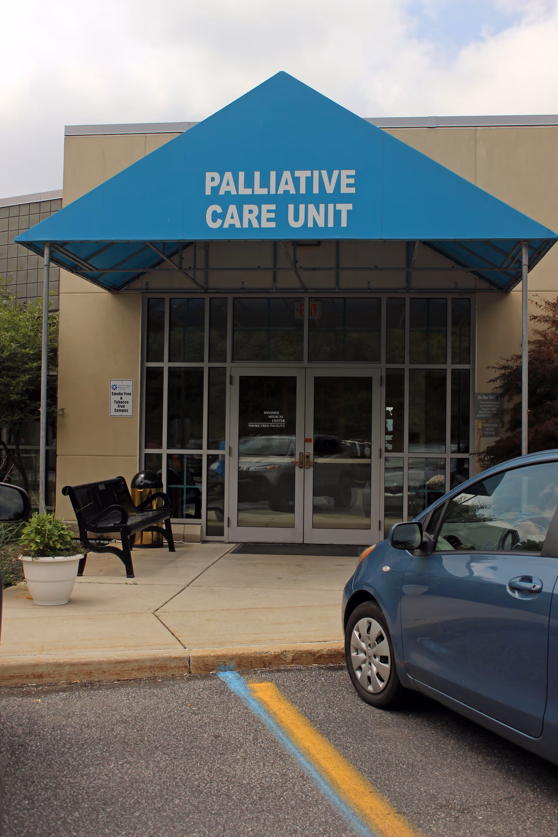 Front entrance of a building with a blue canopy reading PALLIATIVE CARE UNIT