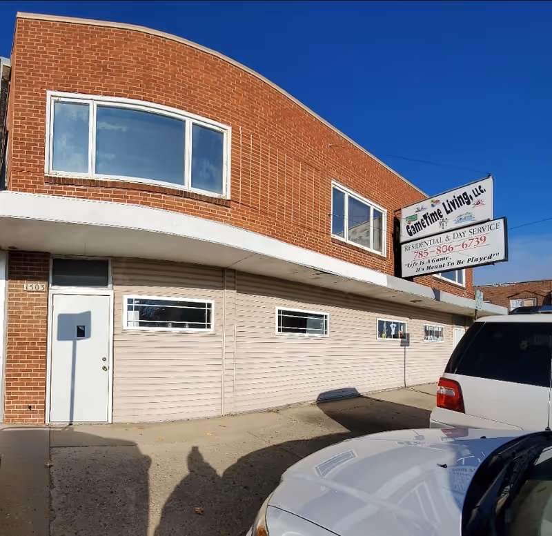 Brick building with curved upper facade and a Gametime Living sign on a sunny day.