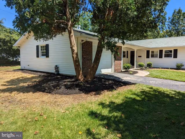White single-story assisted living house with a curved driveway, trees, and manicured lawn.